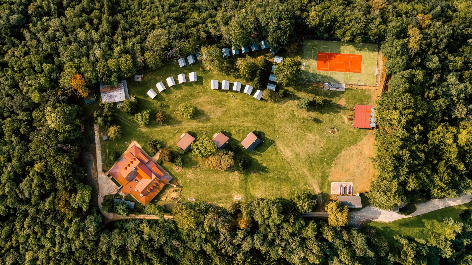 Letecké panorama areálu Na Kamínce s hlavní budovou, loukou a sportovištěm